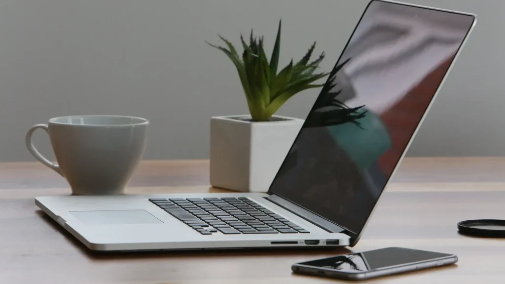 Laptop sitting atop a desk alongside a smartphone and coffee mug