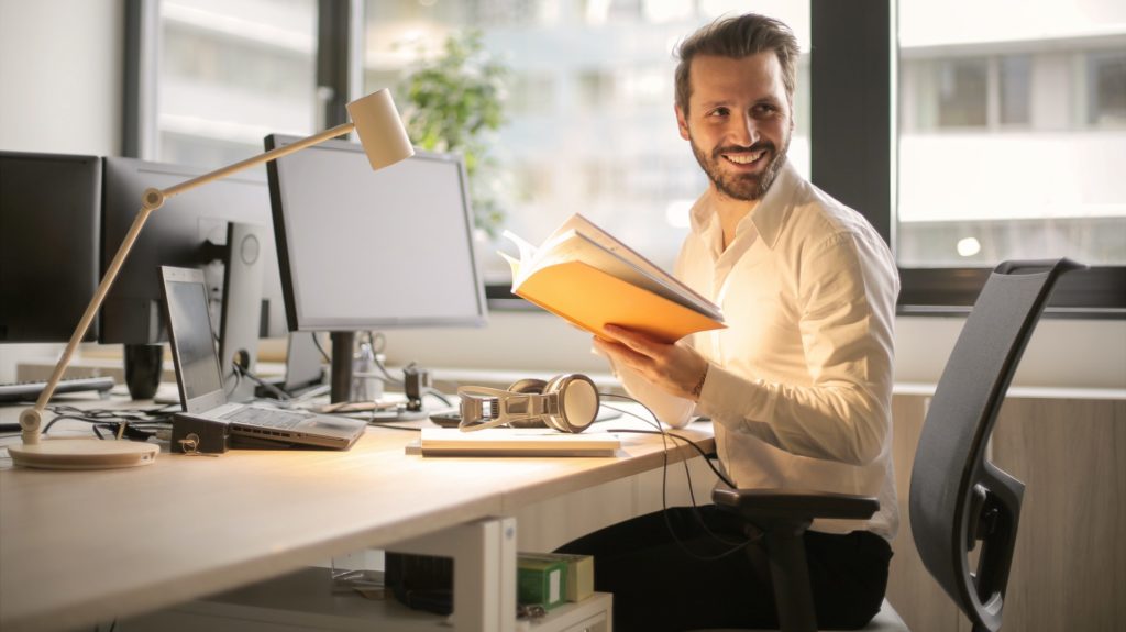 Man sitting at office desk with note book in hand smiling