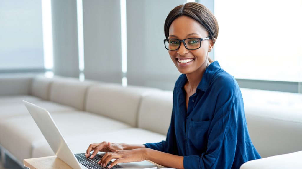 African female with glasses sitting on a couch and working on laptop