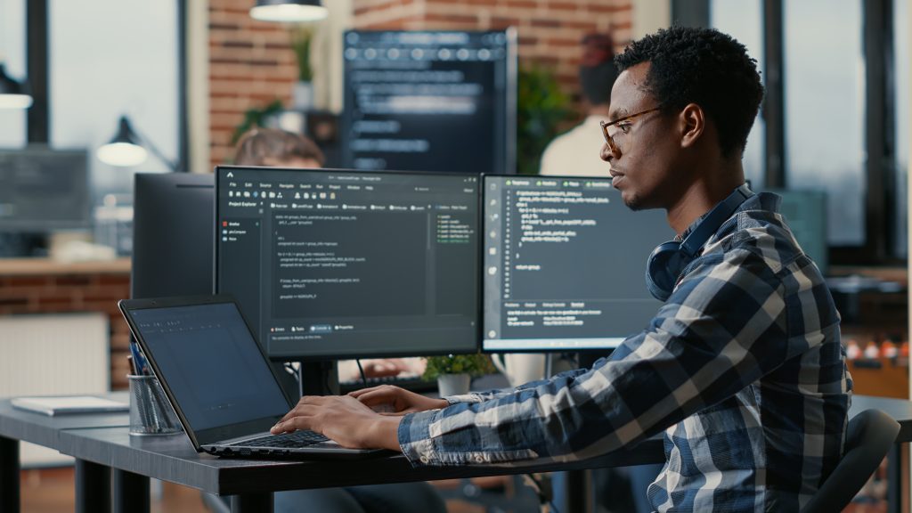 Developer sitting at desk with dual screens programming