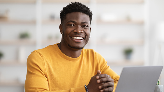 African student sitting a desk with computer open smiling